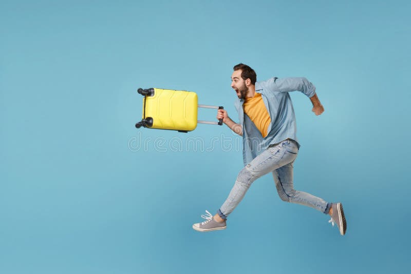 Side view of crazy traveler tourist man in yellow clothes isolated on blue background. Male passenger traveling abroad on weekend. Air flight journey concept. Jumping like running, hold suitcase. Side view of crazy traveler tourist man in yellow clothes isolated on blue background. Male passenger traveling abroad on weekend. Air flight journey concept. Jumping like running, hold suitcase