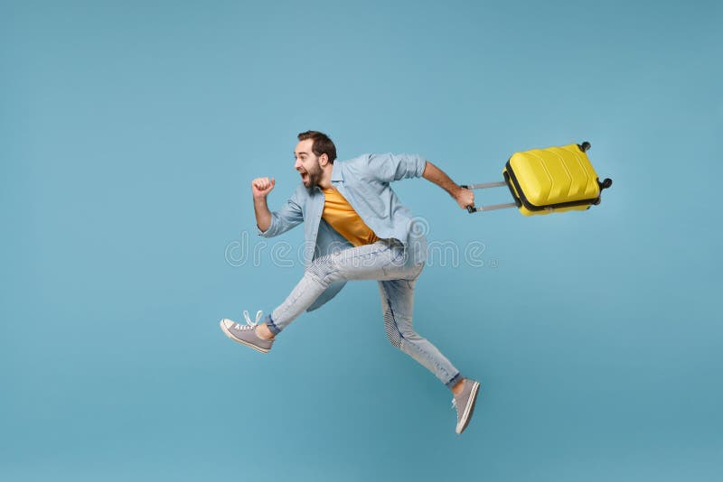 Side view of funny traveler tourist man in yellow clothes isolated on blue background. Male passenger traveling abroad on weekends. Air flight journey concept. Jumping like running, hold suitcase. Side view of funny traveler tourist man in yellow clothes isolated on blue background. Male passenger traveling abroad on weekends. Air flight journey concept. Jumping like running, hold suitcase