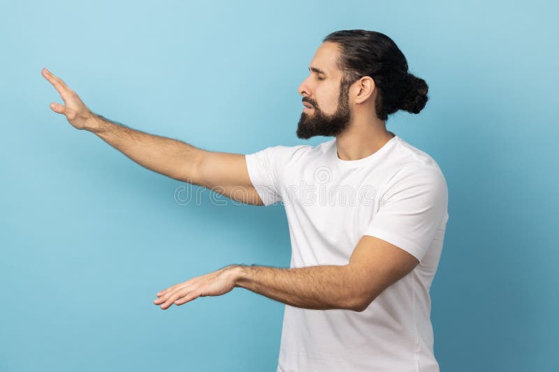 Side view of disoriented blind man with beard wearing white T-shirt standing with stretched arms, searching for way, vision problems. Indoor studio shot isolated on blue background. Side view of disoriented blind man with beard wearing white T-shirt standing with stretched arms, searching for way, vision problems. Indoor studio shot isolated on blue background.