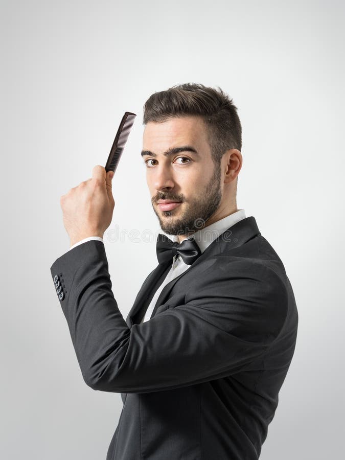 Zijprofielmening van de jonge mens die haar kammen die camera bekijken royalty-vrije stock foto Zijprofielmening van de jonge mens die haar kammen die camera bekijken royalty-vrije stock foto