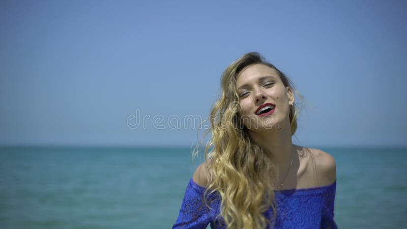 Zingt de blonde jonge vrouw op azuurblauwe kust, strand of kade De sexy meisjeszanger zingt, spreekt, danst, presteert, verleidt