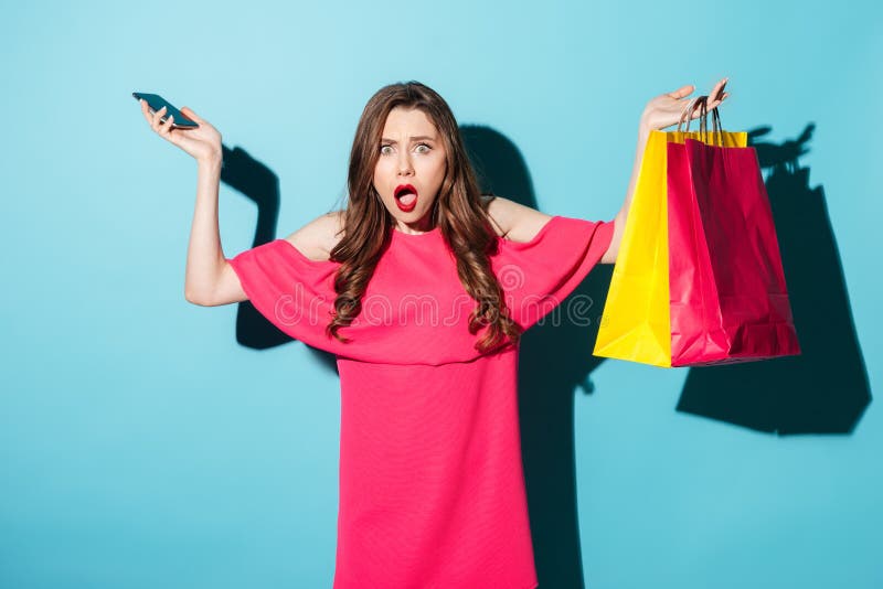 Zmieszany młody brunetki kobiety mienia telefon i torba na zakupy obrazy stock Zmieszany młody brunetki kobiety mienia telefon i torba na zakupy obrazy stock