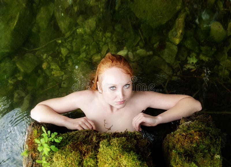 Zmysłowa młoda miedzianowłosa kobiety syrenka jest w dudniący drzewnego bagażnika wyczulony uwodzicielskim z różowymi wodnymi lel fotografia stock Zmysłowa młoda miedzianowłosa kobiety syrenka jest w dudniący drzewnego bagażnika wyczulony uwodzicielskim z różowymi wodnymi lel fotografia stock