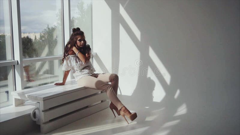 Zmysłowa młodej kobiety brunetka pozuje siedzieć blisko okno