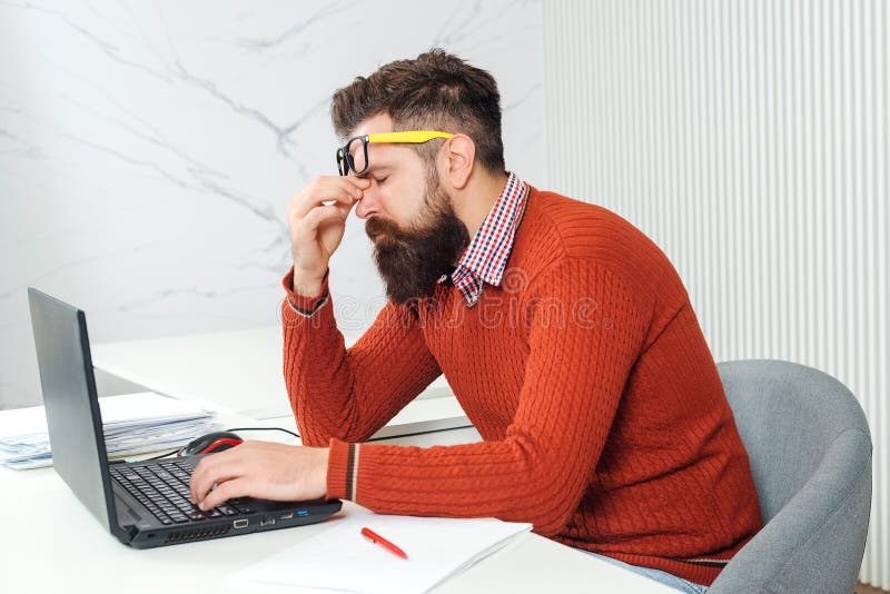 Tired man with laptop computer at working place. Bearded man overworked at office. Stressed handsome business man. Feeling exhausted. Young man having stressful time working on laptop. Tired man with laptop computer at working place. Bearded man overworked at office. Stressed handsome business man. Feeling exhausted. Young man having stressful time working on laptop