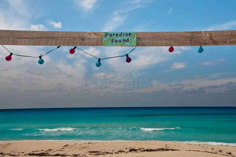 Sign reading Paradise Found on a piece of wood with colorful lights hanging about a beautiful beach in the caribbean. Sign reading Paradise Found on a piece of wood with colorful lights hanging about a beautiful beach in the caribbean