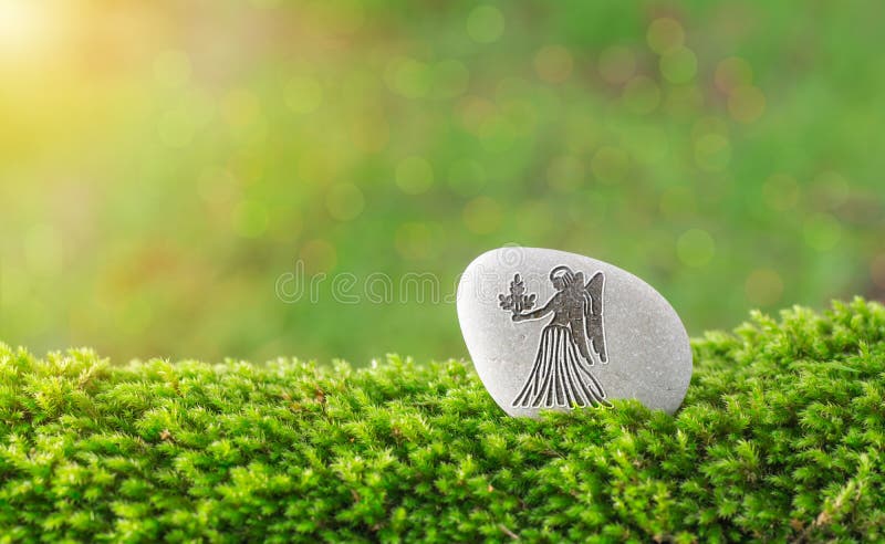 Virgo zodiac symbol in stone on grass with nature bokeh light background. Virgo zodiac symbol in stone on grass with nature bokeh light background