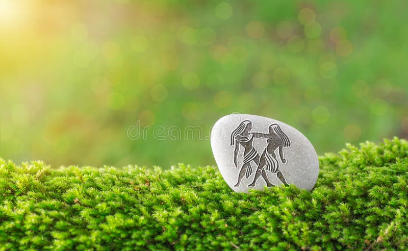 Gemini zodiac symbol in stone on grass with nature bokeh light background. Gemini zodiac symbol in stone on grass with nature bokeh light background