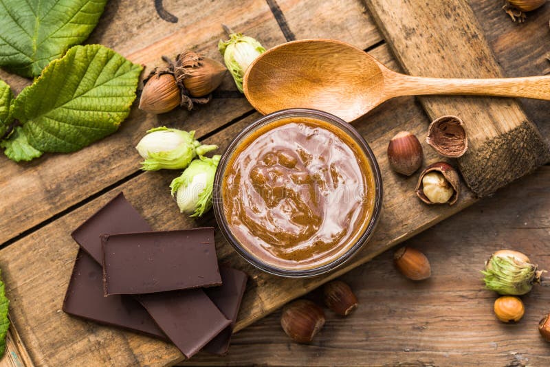 Zoete die chocoladehazelnoot met gehele noten wordt uitgespreid en groene hazelnoot op houten lijst Nutellaroom stock afbeelding Zoete die chocoladehazelnoot met gehele noten wordt uitgespreid en groene hazelnoot op houten lijst Nutellaroom stock afbeelding