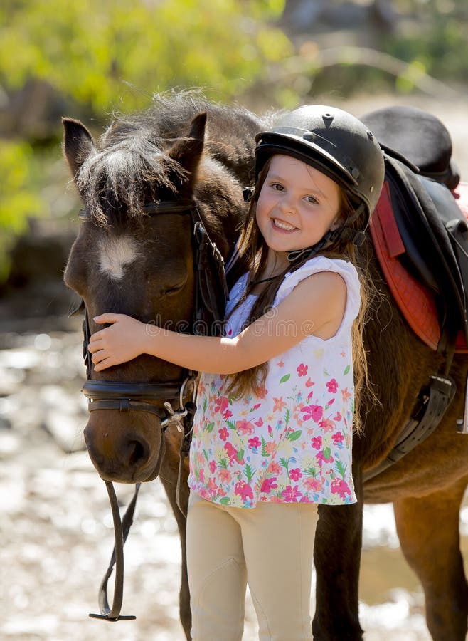 Zoete mooie jong meisje 7 of 8 jaar oud het koesteren hoofd van weinig poneypaard die de gelukkige dragende helm van de veilighei