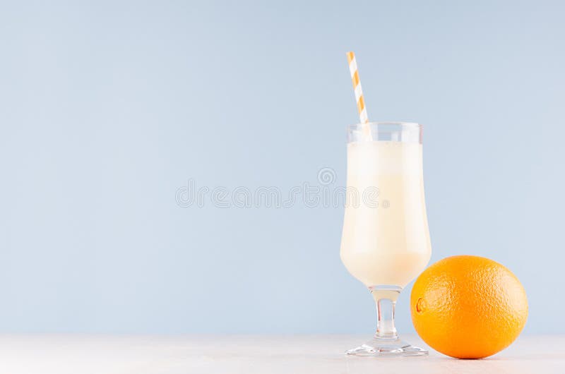 Zoete vrolijke milkshake in glas met geheel oranje en gestreept stro op lichte pastelkleur blauwe achtergrond royalty-vrije stock fotografie Zoete vrolijke milkshake in glas met geheel oranje en gestreept stro op lichte pastelkleur blauwe achtergrond royalty-vrije stock fotografie