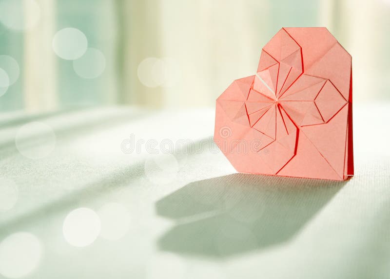 Zonovergoten roze origamidocument hart met schaduw vooraan