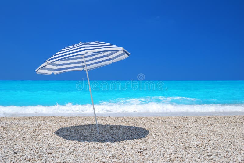 Zonparaplu op een kiezelsteenstrand met turkooise overzees