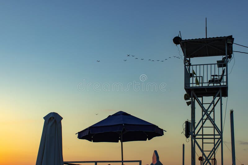 Zonsondergang met de postsilhouet van de het levenswacht De zomerachtergrond royalty-vrije stock fotografie Zonsondergang met de postsilhouet van de het levenswacht De zomerachtergrond royalty-vrije stock fotografie