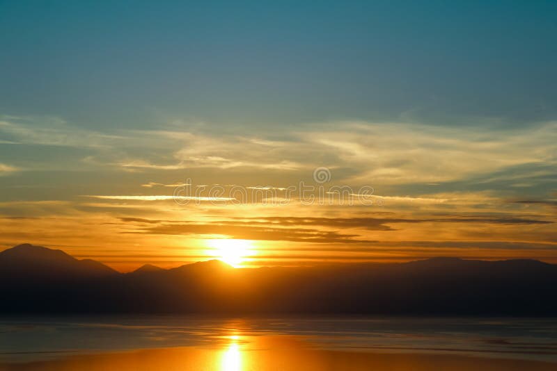 Zonsondergang-zon reeksen achter de bergen en over water met bezinning royalty-vrije stock afbeelding Zonsondergang-zon reeksen achter de bergen en over water met bezinning royalty-vrije stock afbeelding
