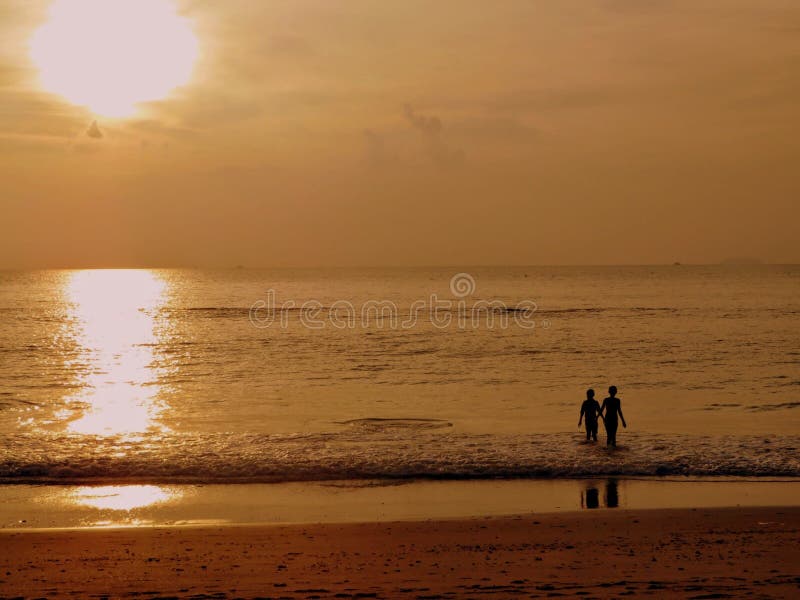 Zonsondergangfoto van een jongen en een meisje die in het overzees lopen terwijl hun gedachtengang op het strand achter hen wordt stock afbeeldingen Zonsondergangfoto van een jongen en een meisje die in het overzees lopen terwijl hun gedachtengang op het strand achter hen wordt stock afbeeldingen