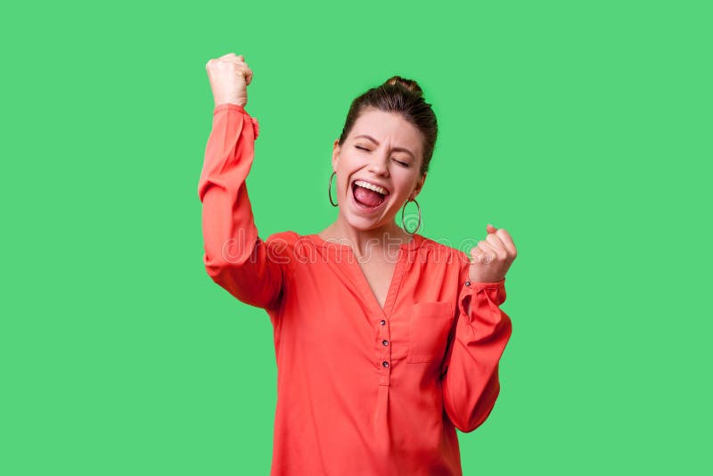 I did it! Portrait of excited winner, beautiful woman with bun hairstyle in red blouse closed eyes and raised hands in happiness, celebrating victory. indoor studio shot isolated on green background. I did it! Portrait of excited winner, beautiful woman with bun hairstyle in red blouse closed eyes and raised hands in happiness, celebrating victory. indoor studio shot isolated on green background