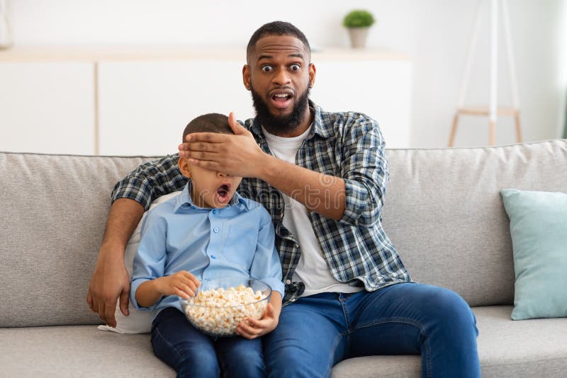 Zszokowany ojciec zasłaniający synów oczy oglądających wątpliwe treści telewizyjne w pomieszczeniach