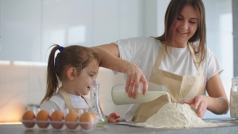 Zu Hause im Küchenmutter- und -tochterbruch ein Ei und Milch dem Mehl für den Kuchen hinzufügen. Hausmannskost und stock video