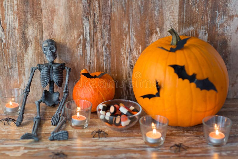 Zucche, scheletro e caramelle di Halloween. Halloween, decorazioni e concetto di feste - zucche con i pipistrelli, lo scheletro e le caramelle su fondo di legno