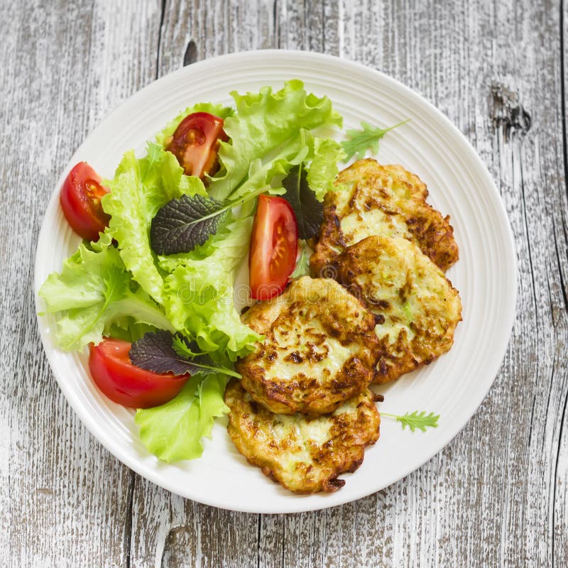 Zucchini bliny i świeżego warzywa sałatka na bielu talerzu obraz stock Zucchini bliny i świeżego warzywa sałatka na bielu talerzu obraz stock