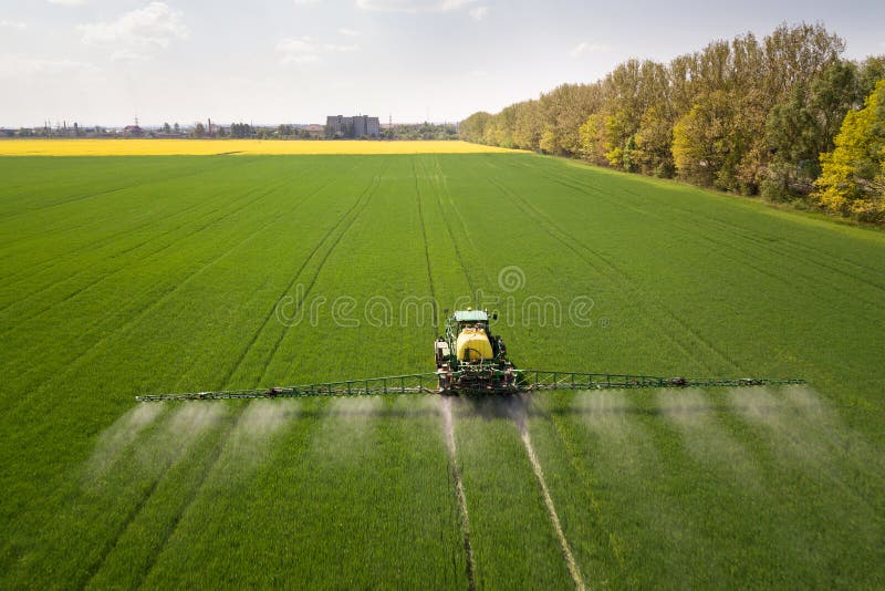 Tractor spraying chemical pesticides with sprayer on the large green agricultural field at spring. Tractor spraying chemical pesticides with sprayer on the large green agricultural field at spring.