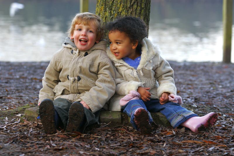 A little blond boy and a mixed race girl sitting resting at the base of a tree. A little blond boy and a mixed race girl sitting resting at the base of a tree.