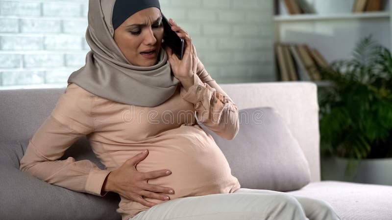 Zwanger moslimwijfje die pijn voelen, die noodsituatiesmartphone, samentrekkingen roepen stock afbeelding Zwanger moslimwijfje die pijn voelen, die noodsituatiesmartphone, samentrekkingen roepen stock afbeelding