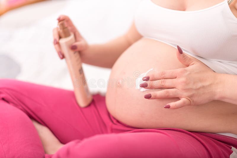 Zwangere vrouw die room op haar buik toepassen stock fotografie Zwangere vrouw die room op haar buik toepassen stock fotografie