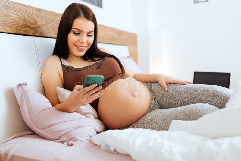 Zwangere vrouw die telefoon met behulp van die op bed liggen royalty-vrije stock afbeeldingen Zwangere vrouw die telefoon met behulp van die op bed liggen royalty-vrije stock afbeeldingen