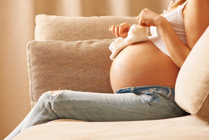 Zwangere vrouw die thuis kleine babyschoenen houden stock fotografie Zwangere vrouw die thuis kleine babyschoenen houden stock fotografie