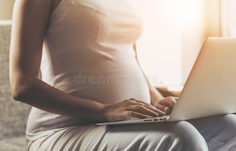 Zwangere Vrouw Gebruikend Laptop en Zittend op Bank stock afbeelding Zwangere Vrouw Gebruikend Laptop en Zittend op Bank stock afbeelding