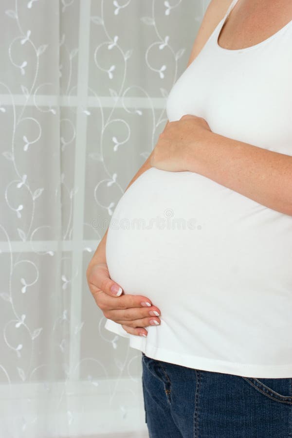 Pregnant woman standing next to a window holding her belly, pregnancy. Pregnant woman standing next to a window holding her belly, pregnancy