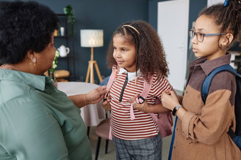 Portrait of little African American girl with backpack getting ready for school in morning with grandmother helping. Portrait of little African American girl with backpack getting ready for school in morning with grandmother helping
