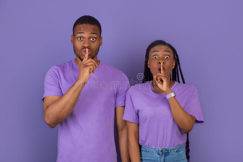 Shh, Keep Silence Concept. Emotional Black Couple Gesturing Hush Sign Posing Standing Isolated Over Purple Violet Studio Wall, Looking Staring At Camera. Holding Finger On Lips, Silent Gesture, Secret. Shh, Keep Silence Concept. Emotional Black Couple Gesturing Hush Sign Posing Standing Isolated Over Purple Violet Studio Wall, Looking Staring At Camera. Holding Finger On Lips, Silent Gesture, Secret