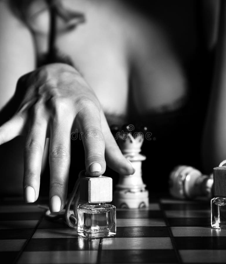 Zwart-wit Sexy vrouw in 'n nachtjurk met diepe ketting die schaak speelt met parfum flessen, die één aanwijst