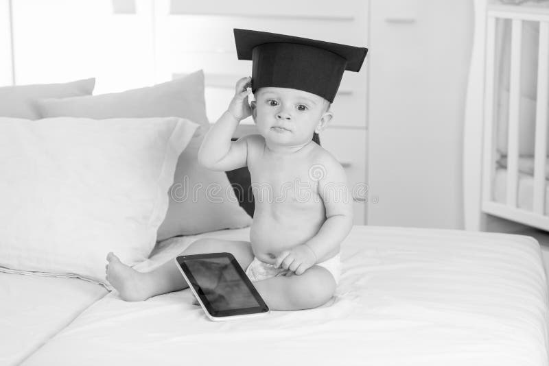 Zwart-witte foto van weinig babyjongen in graduatie GLB die digitale tablet houden stock fotografie Zwart-witte foto van weinig babyjongen in graduatie GLB die digitale tablet houden stock fotografie