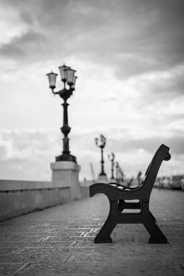 An empty bench against the background of an alley with a lantern in the background. Bari. Italy. An empty bench against the background of an alley with a lantern in the background. Bari. Italy