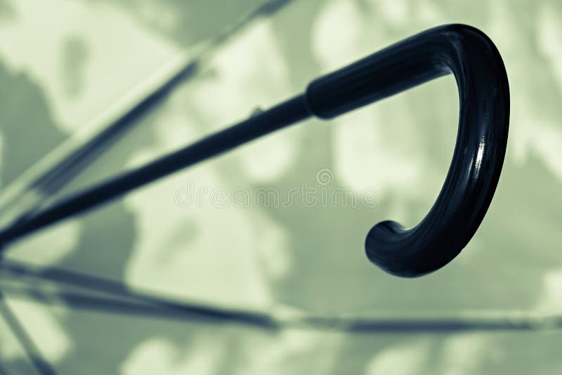 The black umbrella cane handle closeup against an indistinct spotty surface of green color. The black umbrella cane handle closeup against an indistinct spotty surface of green color