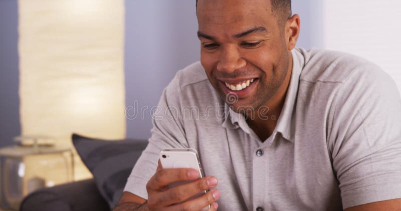 Zwarte mens die en op smartphone glimlachen texting royalty-vrije stock fotografie Zwarte mens die en op smartphone glimlachen texting royalty-vrije stock fotografie