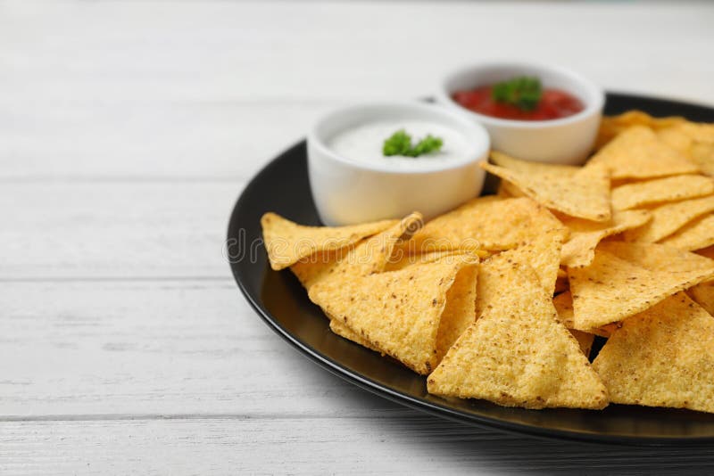 Zwarte plaat met smakelijke Mexicaanse nachos-chips en sauzen op witte houten tafel, klap royalty-vrije stock afbeeldingen Zwarte plaat met smakelijke Mexicaanse nachos-chips en sauzen op witte houten tafel, klap royalty-vrije stock afbeeldingen