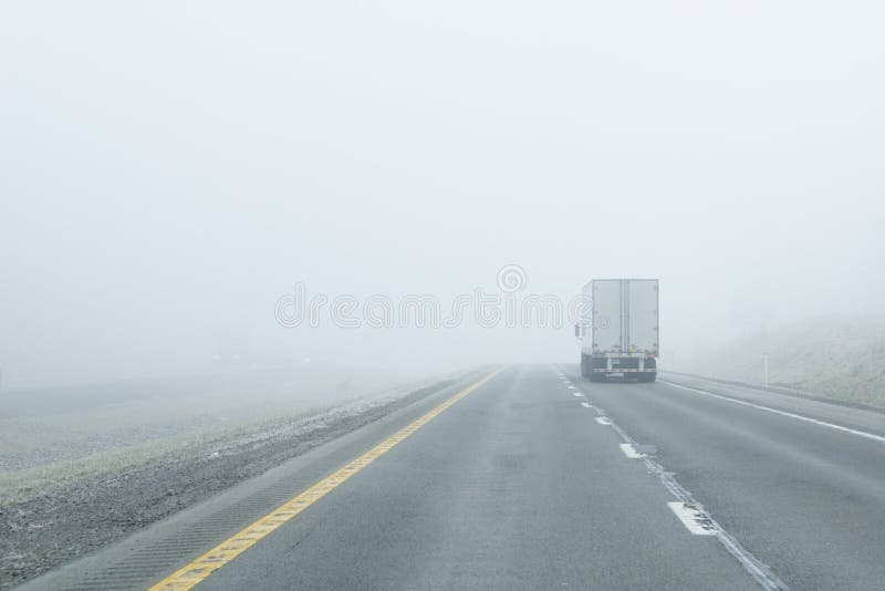 A semi-truck drives into dense fog along an interstate in the mountains. Such dense fog creates can create a dangerous road hazard for any driver. A semi-truck drives into dense fog along an interstate in the mountains. Such dense fog creates can create a dangerous road hazard for any driver.