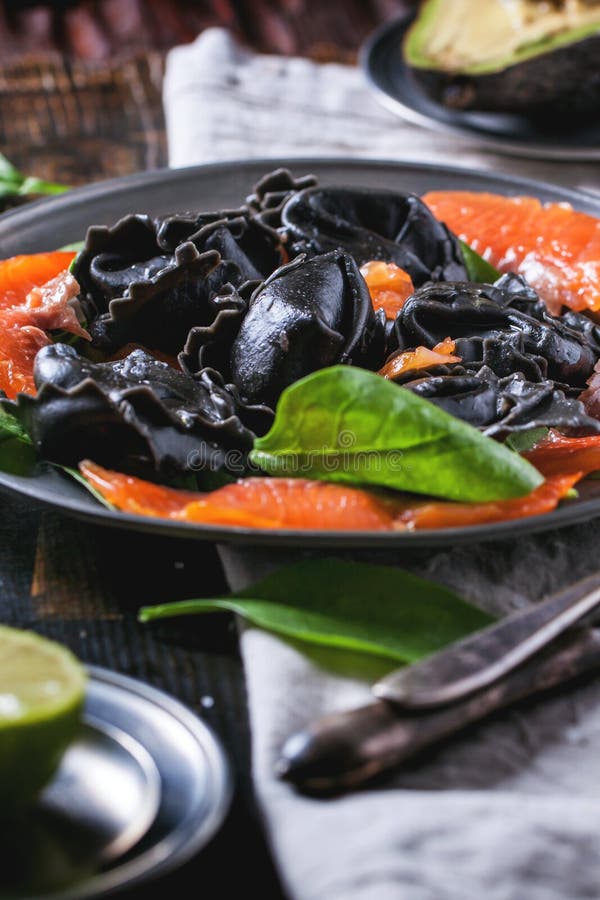 Vintage plate with black homemade ravioli with salted salmon, served on wooden table. Vintage plate with black homemade ravioli with salted salmon, served on wooden table.