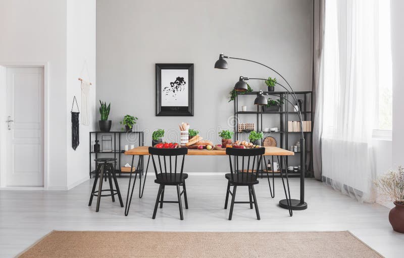 Zwarte stoelen bij eettafel met voedsel in flatbinnenland met lamp en affiche op grijze muur stock foto's Zwarte stoelen bij eettafel met voedsel in flatbinnenland met lamp en affiche op grijze muur stock foto's
