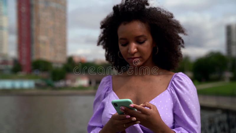 Zwarte vrouw loopt buitenshuis en doorbladert sociale netten op smartphone