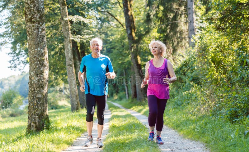 Full length front view of two active seniors with a healthy lifestyle smiling while jogging together outdoors in the park. Full length front view of two active seniors with a healthy lifestyle smiling while jogging together outdoors in the park