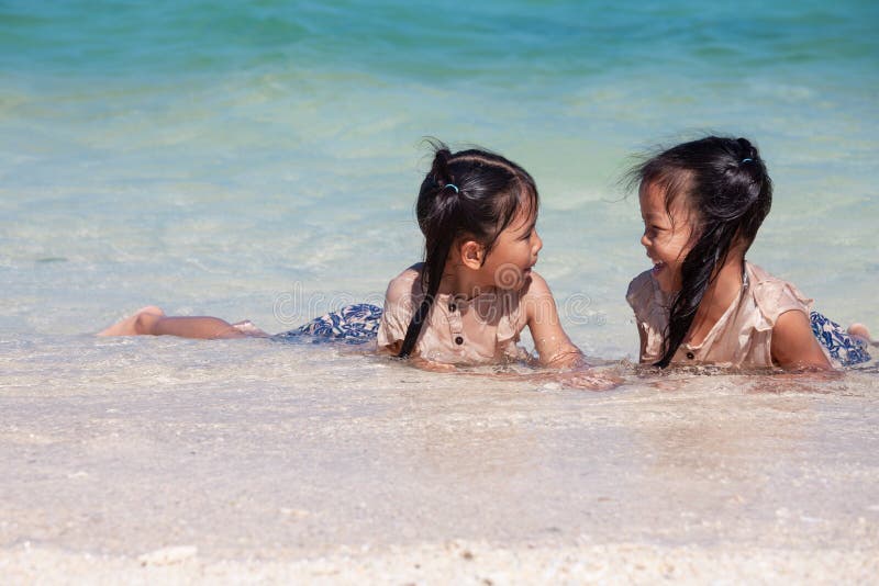 Zwei asiatische Kindermädchen, die den Spaß, zum des Wassers im schönen Meer in den Sommerferien zusammen zu spielen haben lizenzfreie stockfotografie