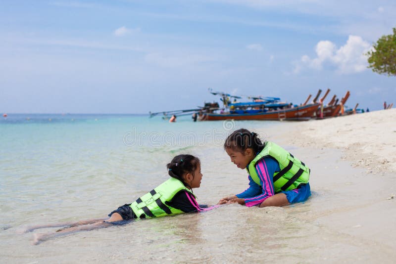 Zwei asiatische Kindermädchen, welche die Schwimmweste spielt Wasser im schönen Meer zusammen mit Spaß in den Sommerferien tragen lizenzfreies stockbild