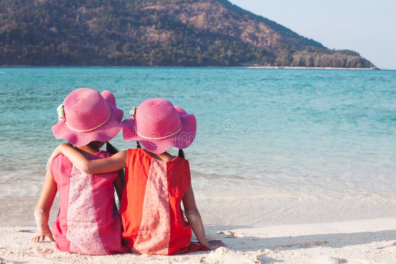 Zwei asiatische kleines Kindermädchen, die auf dem Strand nahe dem schönen Meer in den Sommerferien sitzen und sich umarmen stockfotografie