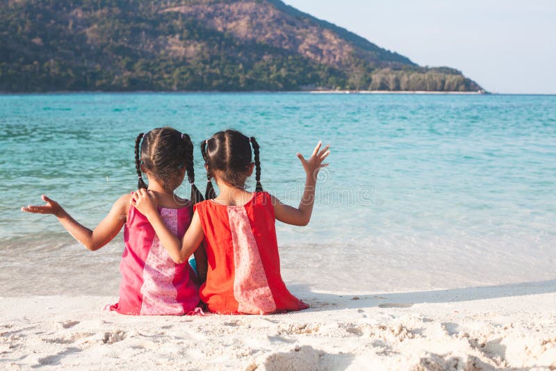 Zwei asiatische kleines Kindermädchen, die zusammen auf dem Strand nahe dem schönen Meer in den Sommerferien sitzen und spielen stockfotos